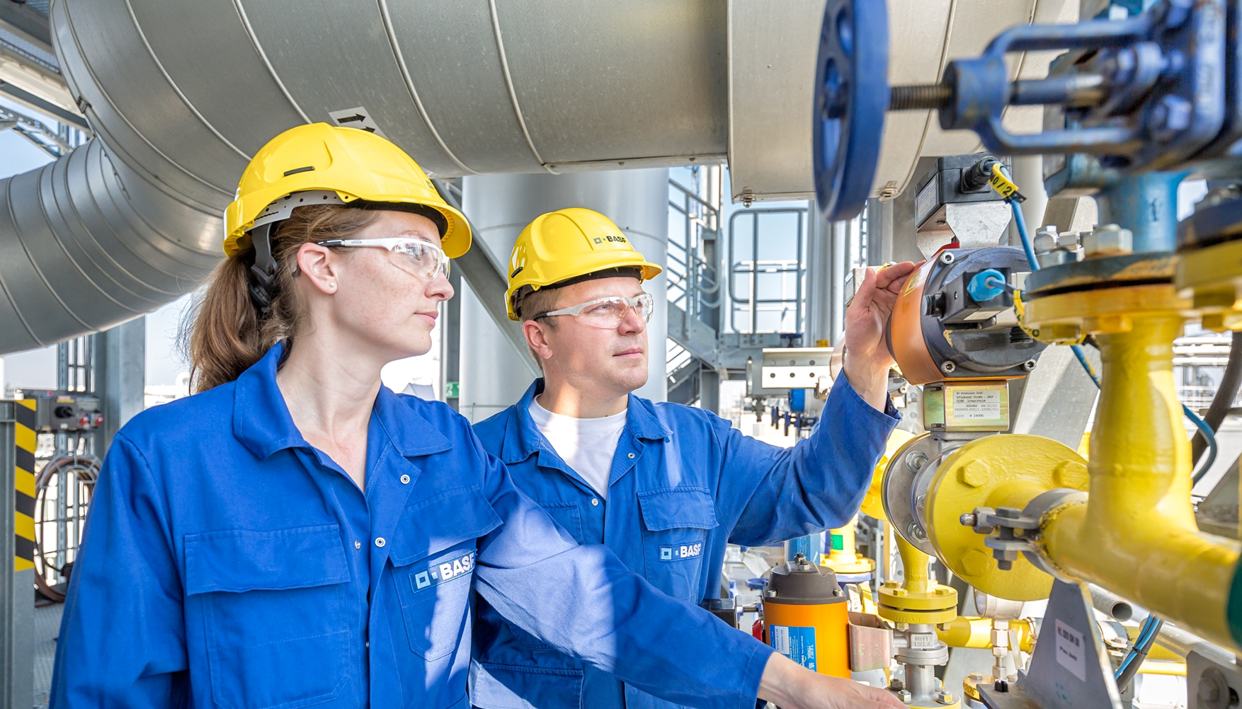 Arbeitsfachkräfte (Frau und Mann) mit Blick auf Industrieanlage