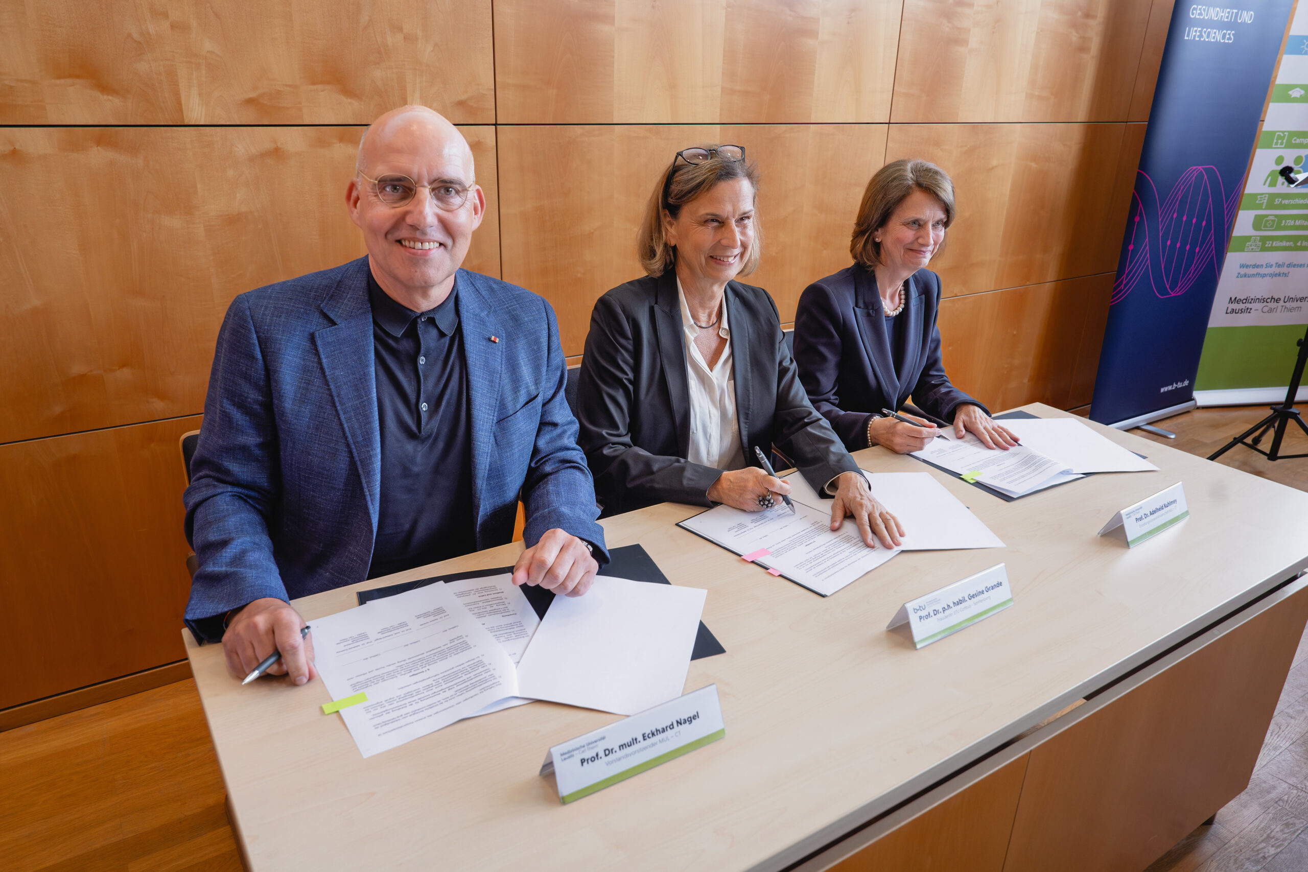 Prof. Dr. Eckhard Nagel, Prof. Dr. Gesine Grande und Prof. Dr. Adelheid Kuhlmey sitzen im Podium und unterschreiben die Kooperationsvereinbarung
