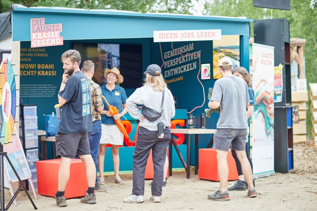 Eventstand "Krasse Lausitz" beim Feel Festival. Einige Besucher:innen im Gespräch