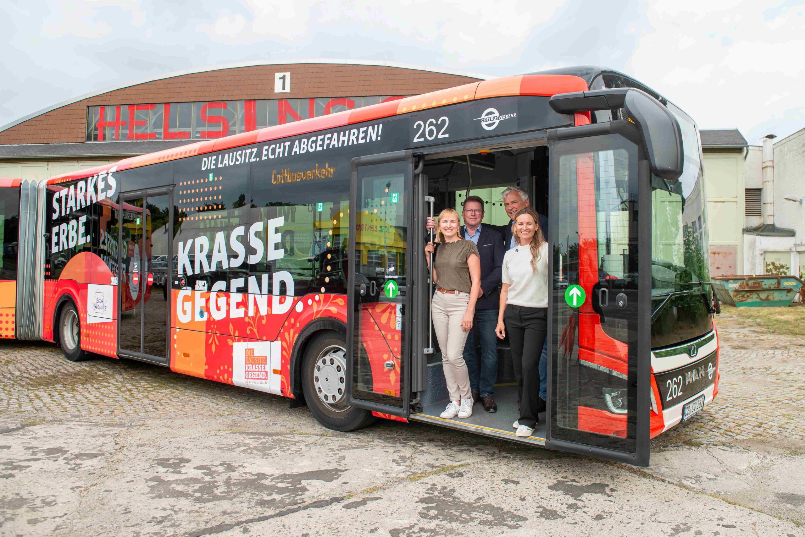Busbeklebung "Starkes ERbe. Krasse Gegend." Aus der geööfneten Tür schauen Heiko Jahn, Dr. Freytag, Maria Schulz und Susann Troppa