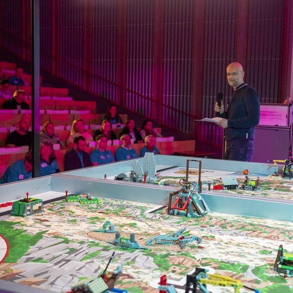 BTU-Vizepräsident eröffnet mit Mikro und Blick auf das Spielfeld die Veranstaltung.  Im Hintergrund sind Teilnehmer im Hörsaal sitzend zu sehen