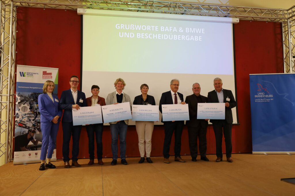 Gruppenfoto auf dem Podium mit den Projektinitiatoren, die ein übergroßen Zuwendungsbescheid in den Händen halten