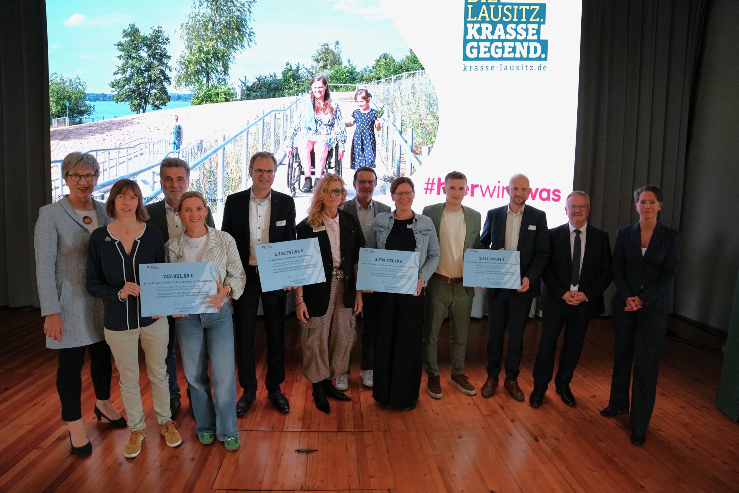 Gruppenfoto mit den vier Zuwendungsbescheidempfängern und einen symbolischen Check in der Hand